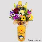 Botella de Pisco Sour Mango maracuyá con arreglo floral vibrante.